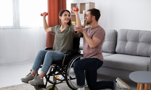 Disability support worker assisting a wheelchair user with light exercise at home