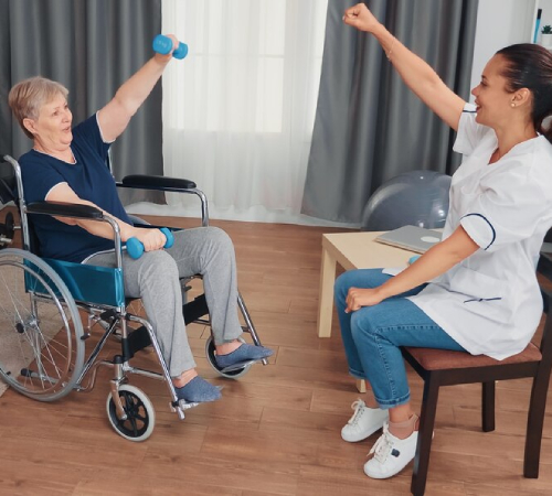 Care worker assisting an older woman in a wheelchair with light exercise and physical activity